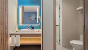 Un baño moderno con un espejo grande, un lavabo blanco y una cabina de ducha de vidrio.