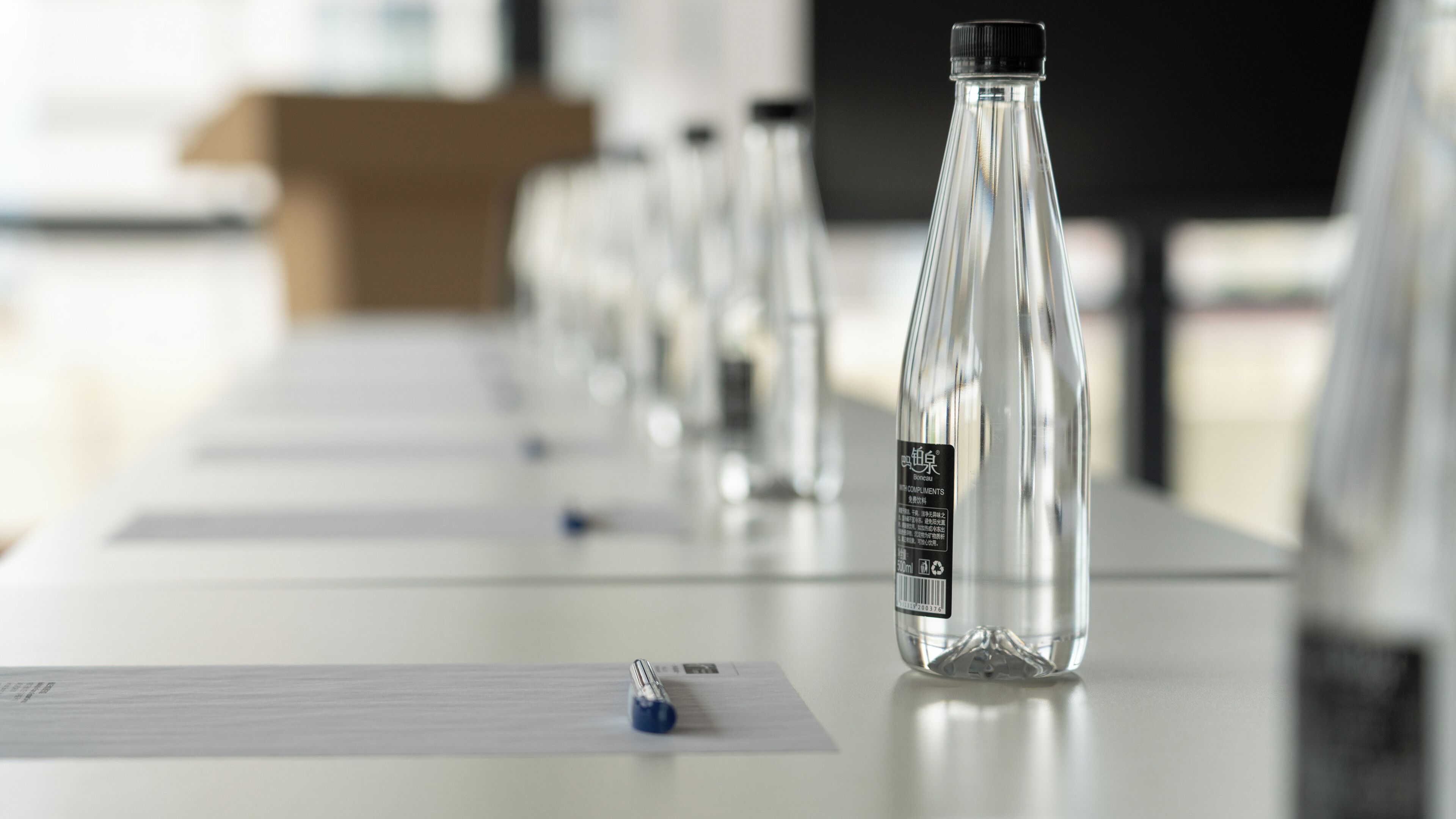 Une rangée de bouteilles en verre transparentes est posée sur une table, à côté d’une étiquette, d’un stylo et d’une feuille de papier.