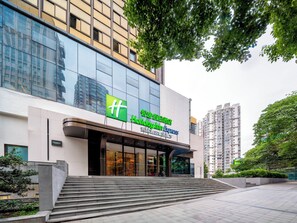 Een modern gebouw met een grote glazen gevel, een opvallend groen en wit Holiday Inn Express bord, en een trap die naar de ingang leidt.