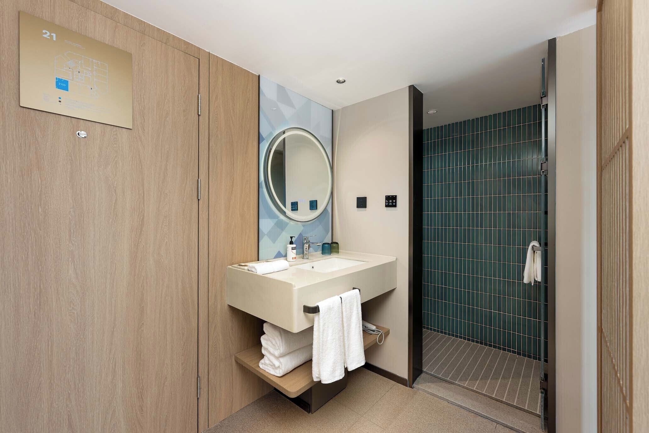 Une salle de bain moderne avec un meuble-lavabo en bois, un grand miroir, un lavabo et un espace douche.