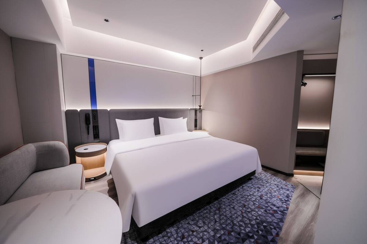 Une chambre d’hôtel moderne avec un grand lit, une table de chevet, une chaise et un tapis à motifs.