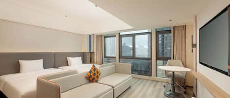 Una habitación de hotel moderna con sofá cama, escritorio y un amplio ventanal con vistas a la ciudad.