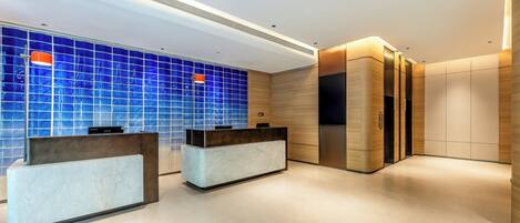 Un área de recepción moderna con dos mostradores, un muro con azulejos azules y un panel de madera.