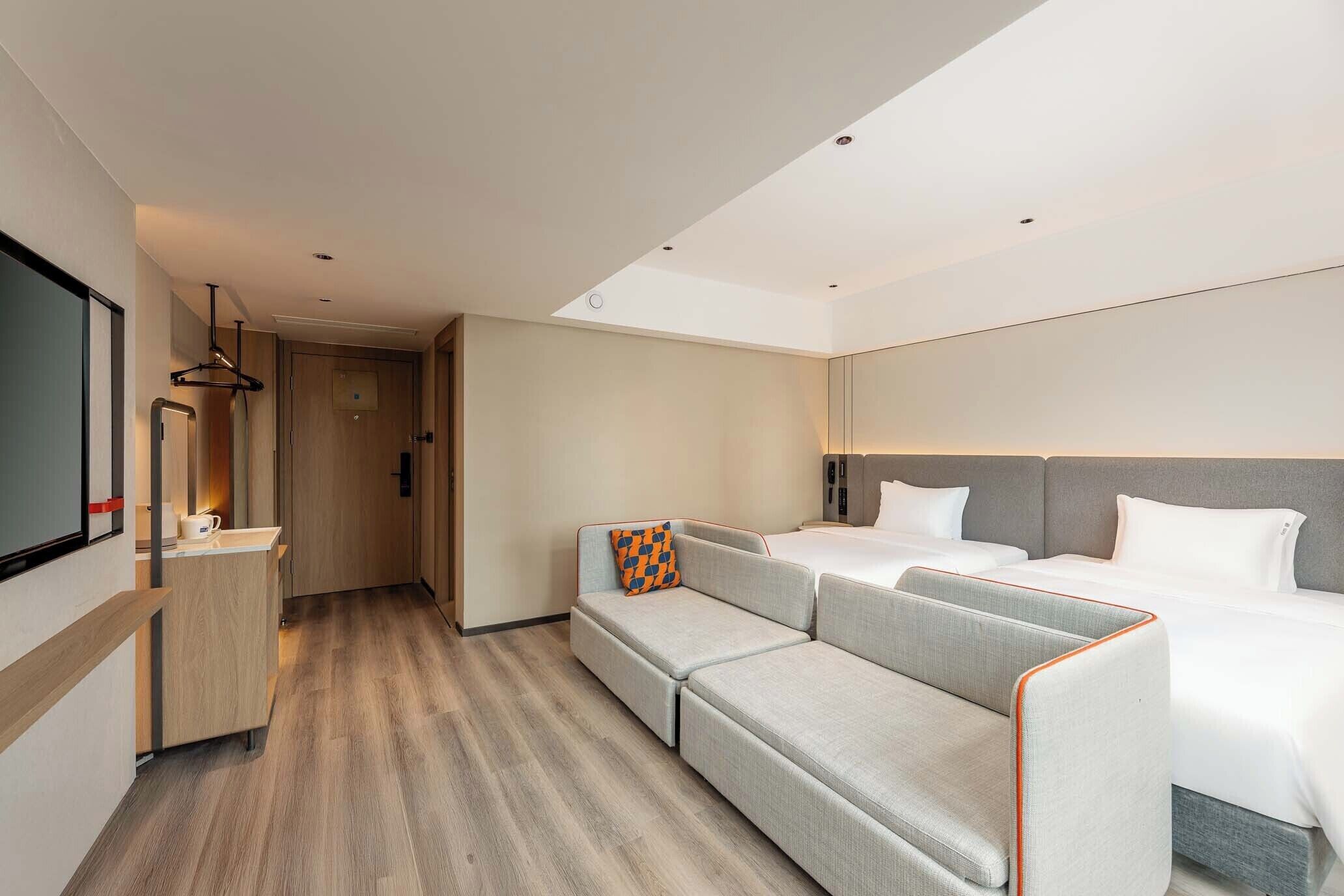 A modern hotel room with a sofa bed, a desk, and a flat-screen TV.