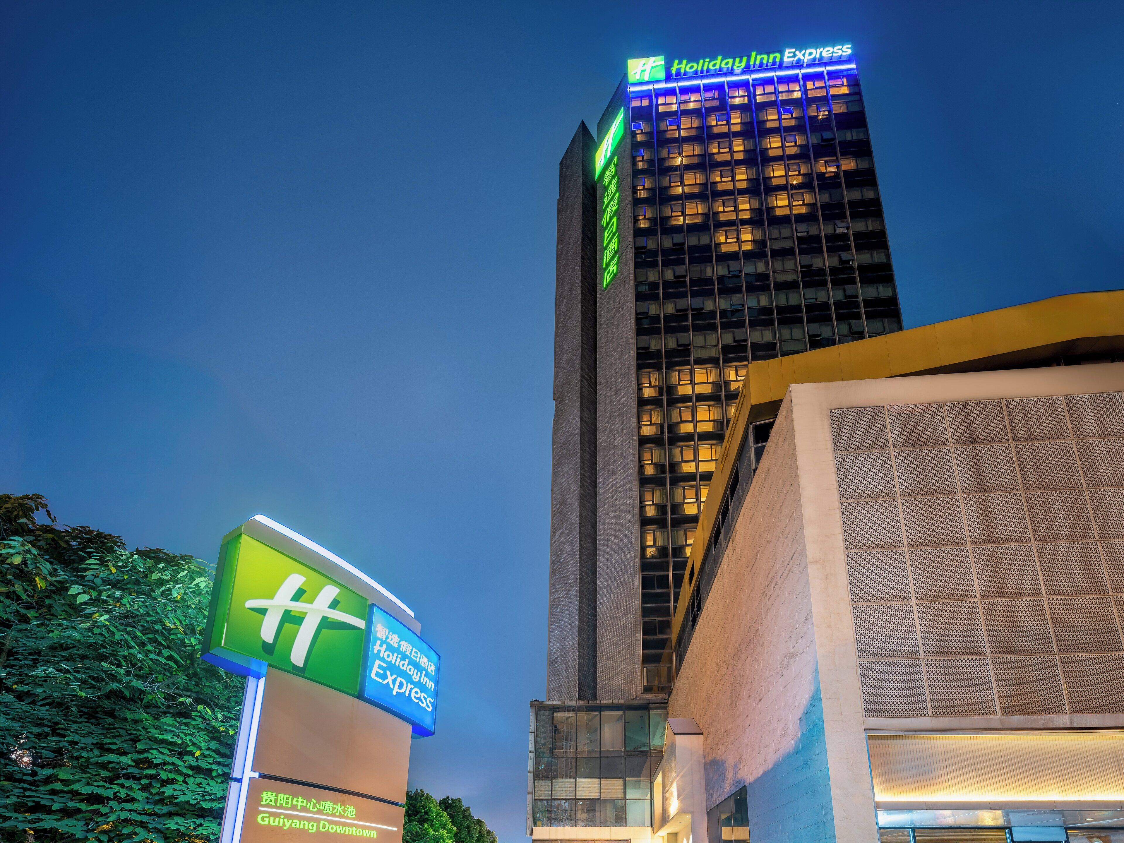 A Holiday Inn Express building with a prominent sign, surrounded by greenery and other buildings.