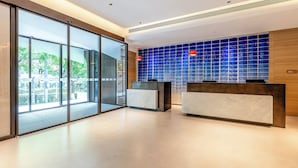 Un espace d’accueil moderne avec des portes vitrées donnant sur un espace extérieur, un comptoir d’accueil et un mur recouvert de carreaux bleus.