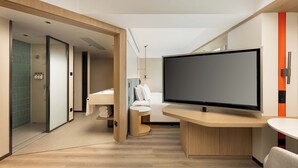 Une chambre d’hôtel moderne dotée d’un grand téléviseur à écran plat, d’une petite table ronde, d’un canapé et d’un espace salle de bain séparé.