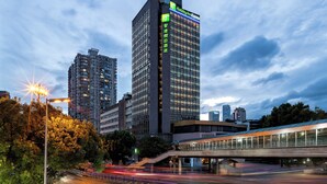 Un hôtel moderne, reconnaissable à son enseigne imposante, sa façade en verre et son pont piétonnier.
