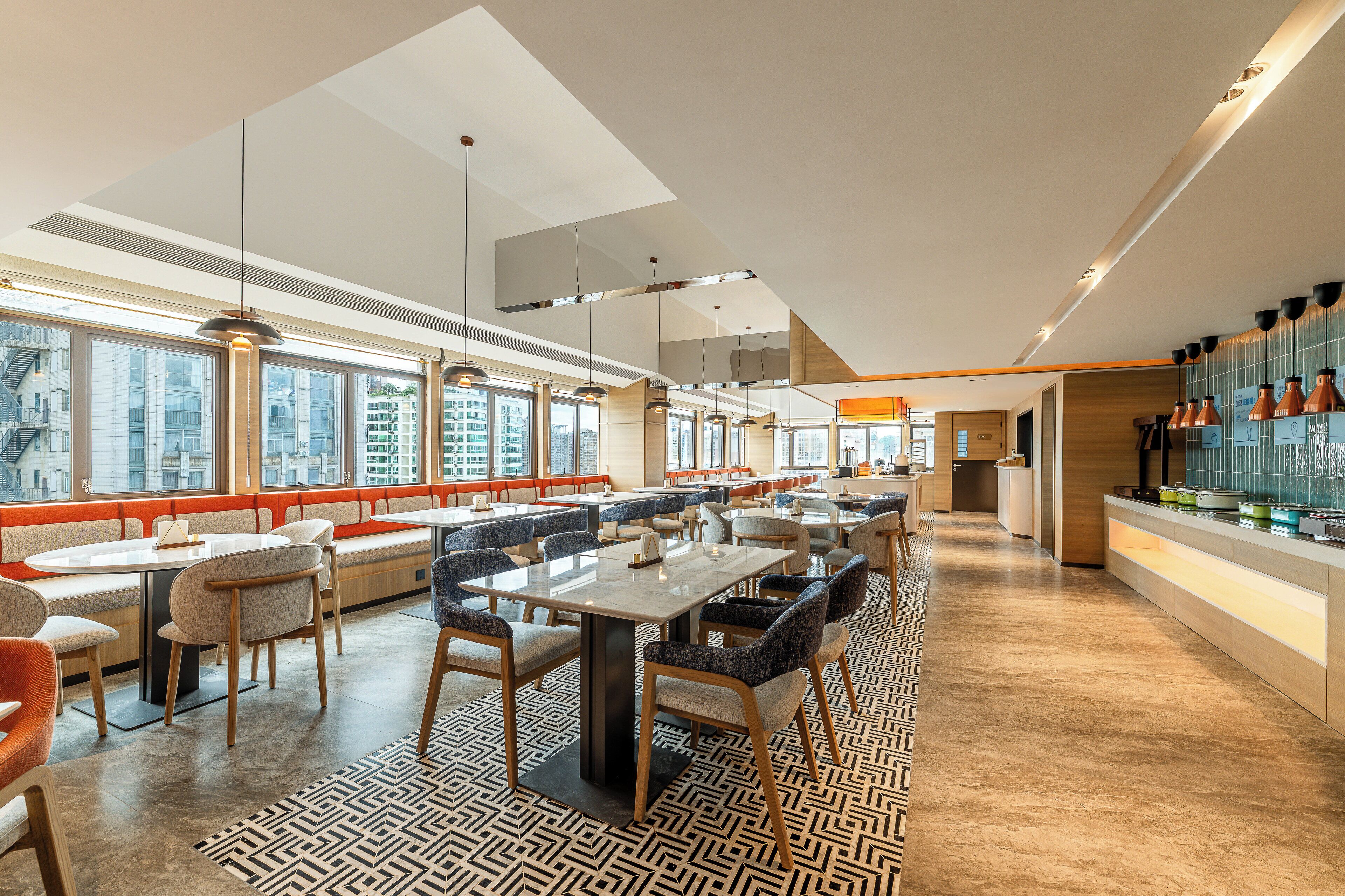 Un restaurante moderno con techos altos, amplias ventanas y una variedad de opciones de asientos, incluyendo mesas y cabinas.