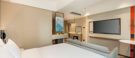 A modern hotel room with a large bed, a TV, a small desk, and a seating area.