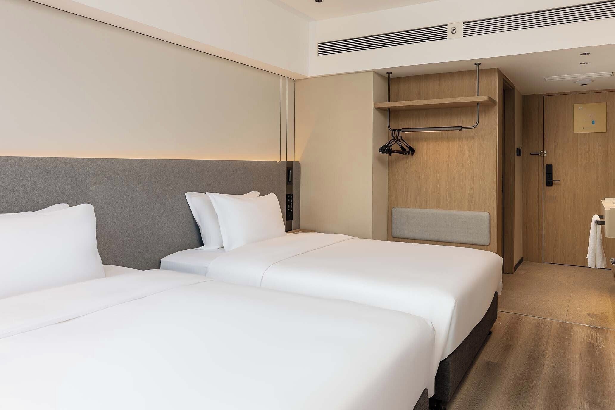 Habitación de hotel con dos camas, un armario de madera, un perchero y un baño pequeño.