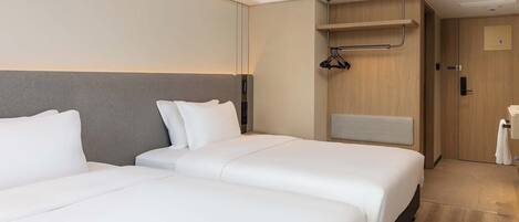 Habitación de hotel con dos camas, un armario de madera, un perchero y un baño pequeño.