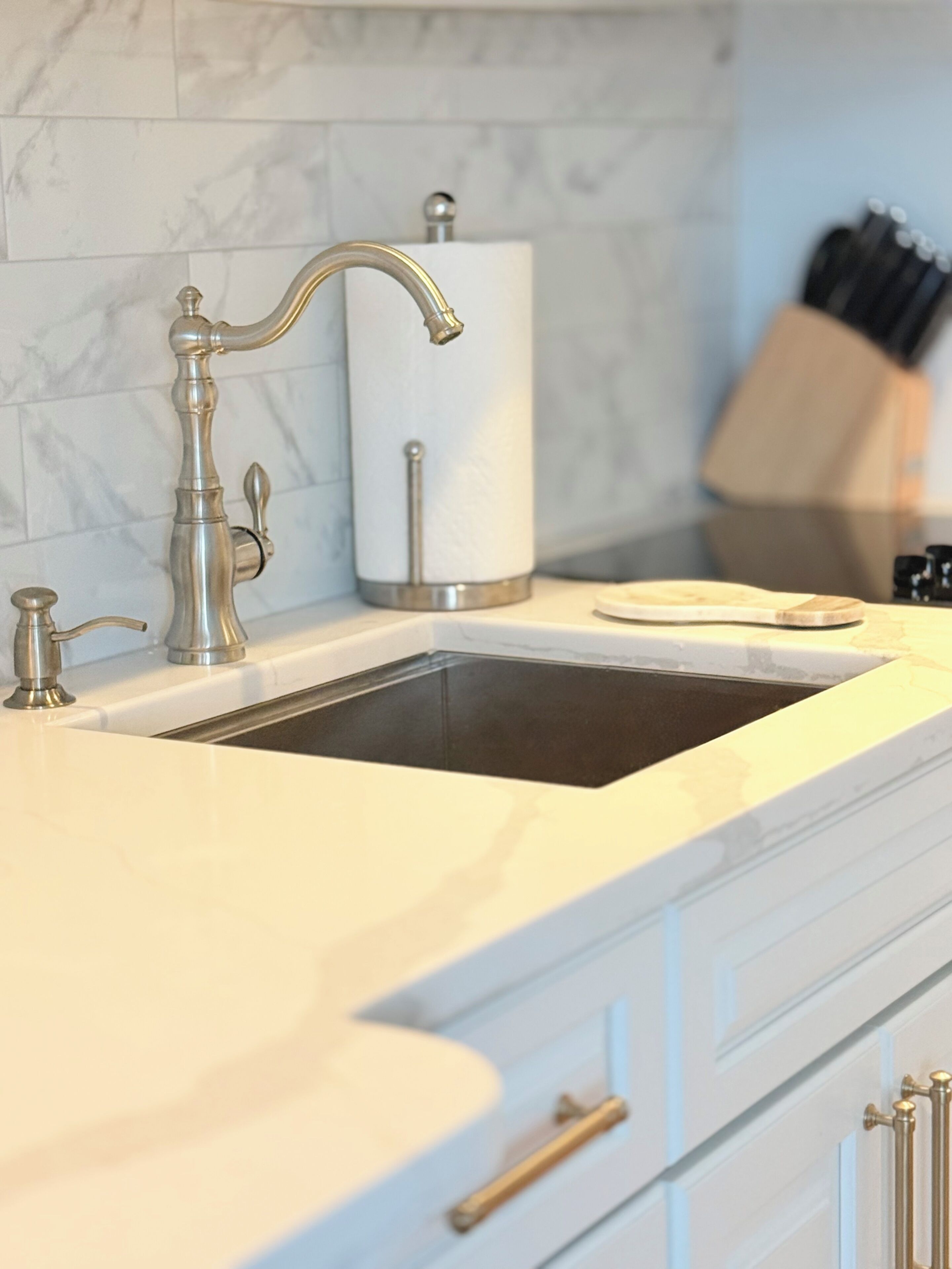 A kitchen with a sink, faucet, and marble backsplash.