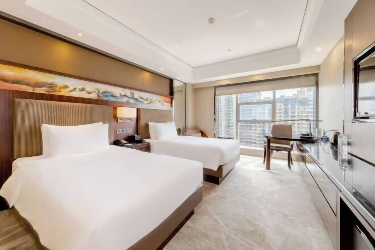 Ein Hotelzimmer mit zwei Betten, einem Schreibtisch, einem Stuhl, einem Fernseher und einem großen Fenster.