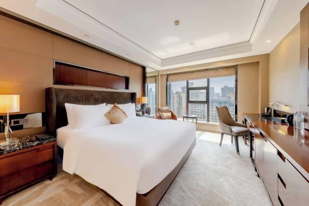 Ein modernes Hotelzimmer mit einem großen Bett, einem Schreibtisch und Blick auf die Stadt.