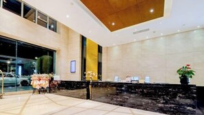 Un hall d’hôtel moderne avec un comptoir d’accueil, une grande fenêtre et une plante décorative.