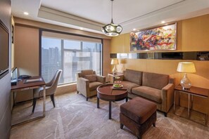 A modern hotel room with a desk, two armchairs, a sofa, a coffee table, and a TV. - Grand Noble Hotel (Chengdu)