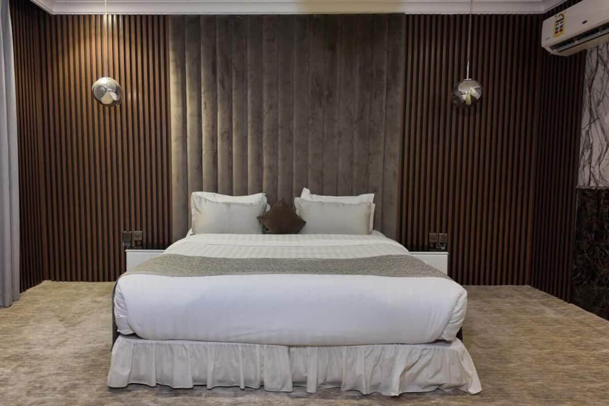 A modern bedroom with a large bed, wooden panel walls, and a marble accent wall.
