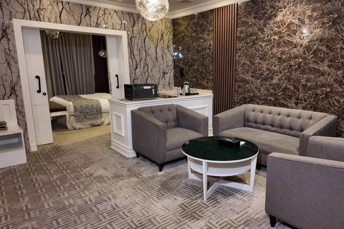 A modern room with a bed, two armchairs, a small table, and a desk with a computer.