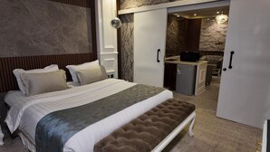 A bedroom with a large bed, a bench, a wardrobe, and a kitchenette area. - Elaf Dammam Serviced Apartment (Dammam)