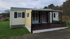 A small, single-story mobile home with a porch and a covered outdoor area. - Mobile home in the heart of nature (Minzac)