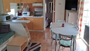 A compact kitchen with a microwave, toaster, and stove, a dining area with a table and chairs, and a small sofa. - Mobile home in the heart of nature (Minzac)