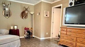 A living room with a sofa, a television on a wooden cabinet, and two deer head wall decorations.