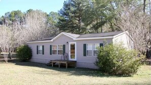 A single-story house with a front porch, a small deck, and a lawn.