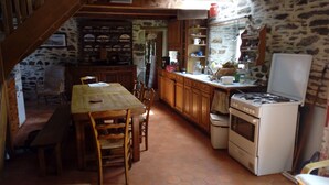 A rustic kitchen with wooden cabinets, a tiled floor, and a stove. - Traditional farmhouse with large garden. Porsliogan beach 500m away on foot. (Le Conquet)