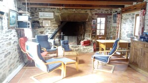 A rustic interior with stone walls, a fireplace, and wooden furniture including chairs and a table. - Traditional farmhouse with large garden. Porsliogan beach 500m away on foot. (Le Conquet)