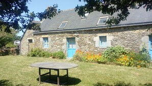 A stone building with a blue door and windows, a round table in the foreground, and a grassy lawn. - Traditional farmhouse with large garden. Porsliogan beach 500m away on foot. (Le Conquet)
