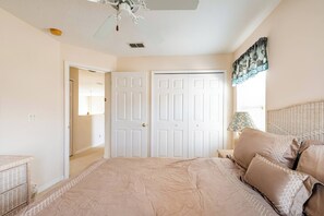 A bedroom with a bed, two doors, a ceiling fan, a window with curtains, and a nightstand with a lamp.