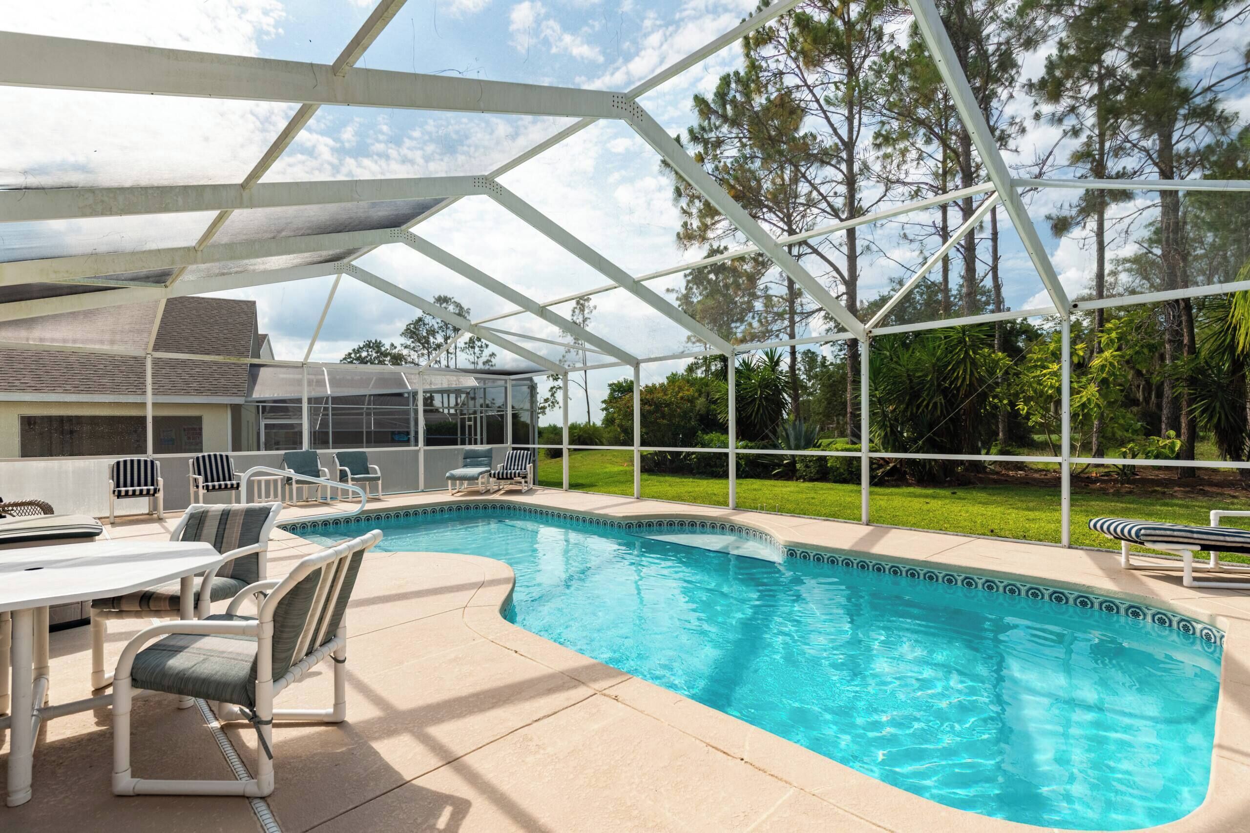 A covered outdoor swimming pool with lounge chairs and a patio table.
