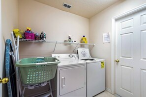 A laundry room with a washing machine, dryer, and shelves with cleaning supplies.