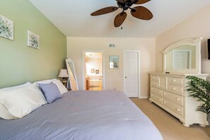 A bedroom with a bed, dresser, ceiling fan, and a door leading to a bathroom.
