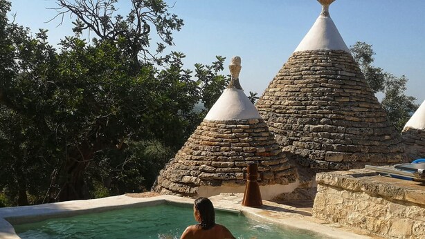 Una persona en una piscina de piedra con techos cónicos al fondo.