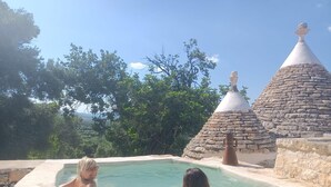 Zona de piscina con estructuras de piedra y vistas a árboles y montañas.