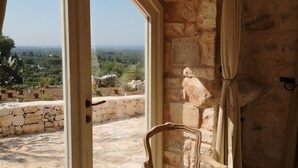 Habitación con paredes de piedra, un gran ventanal de arco, una silla de madera y vistas al paisaje.