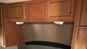 A compact RV interior with a bed, wooden cabinets, and overhead lighting. - 1-bedroom RV in lovely Leona with a lake to fish and swim!! Exotic animals!! (Leona)