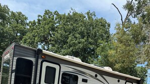 A Trail Runner RV parked on grass with a wooded area in the background. - 1-bedroom RV in lovely Leona with a lake to fish and swim!! Exotic animals!! (Leona)