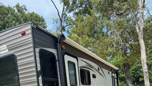 A recreational vehicle with a sliding door, a small step-up ramp, and a flatbed at the back. - 1-bedroom RV in lovely Leona with a lake to fish and swim!! Exotic animals!! (Leona)