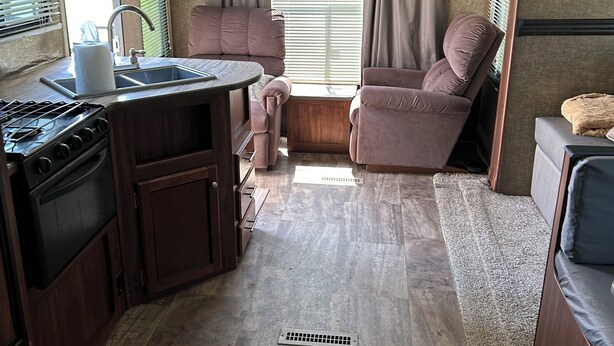 A compact RV kitchen with a stove, sink, and cabinets. There is a seating area with a couch and a small table. - 1-bedroom RV in lovely Leona with a lake to fish and swim!! Exotic animals!! (Leona)