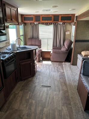 A compact RV kitchen with a stove, sink, and cabinets. There is a seating area with a couch and a small table.