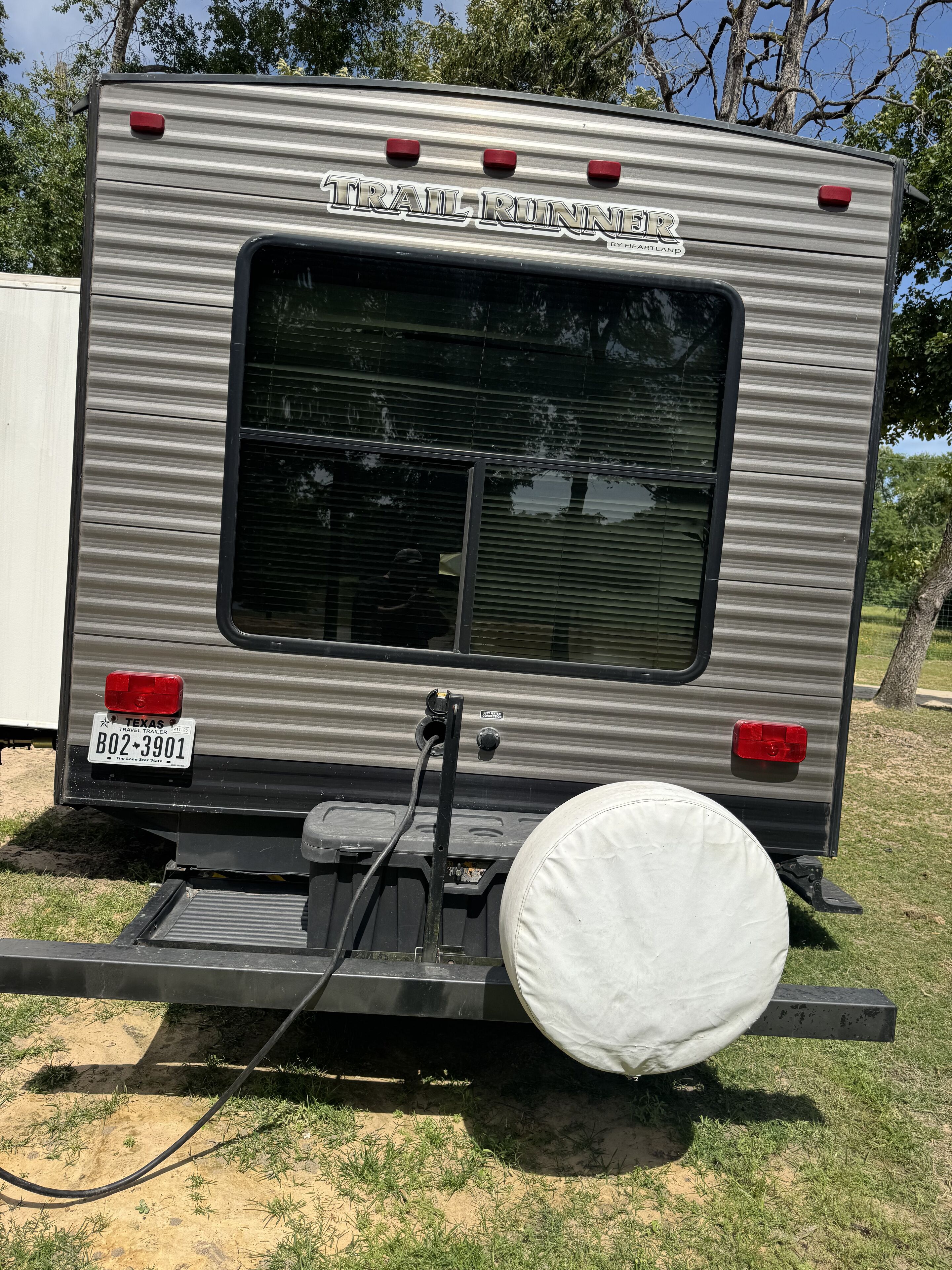 A travel trailer with a window, a license plate, and a white cover on the back.