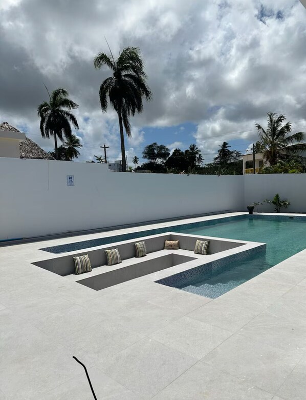 Relax by the rectangular pool surrounded by a light-colored deck and palm trees.