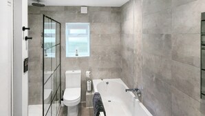 Een moderne badkamer met een douchecabine van glas, een toilet, een bad en een raam voor natuurlijk licht.
