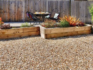 Eine Terrasse mit Holztisch und -stühlen, umgeben von erhöhten Blumenbeeten mit verschiedenen Pflanzen.