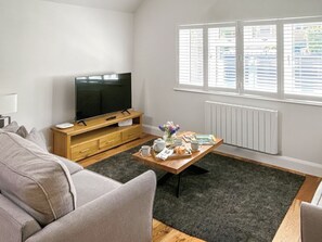 Ein Wohnzimmer mit einer Couch, einem Couchtisch mit einer Platte voller Speisen, einem Fernseher auf einem Holzgestell und einem Fenster mit Jalousien.