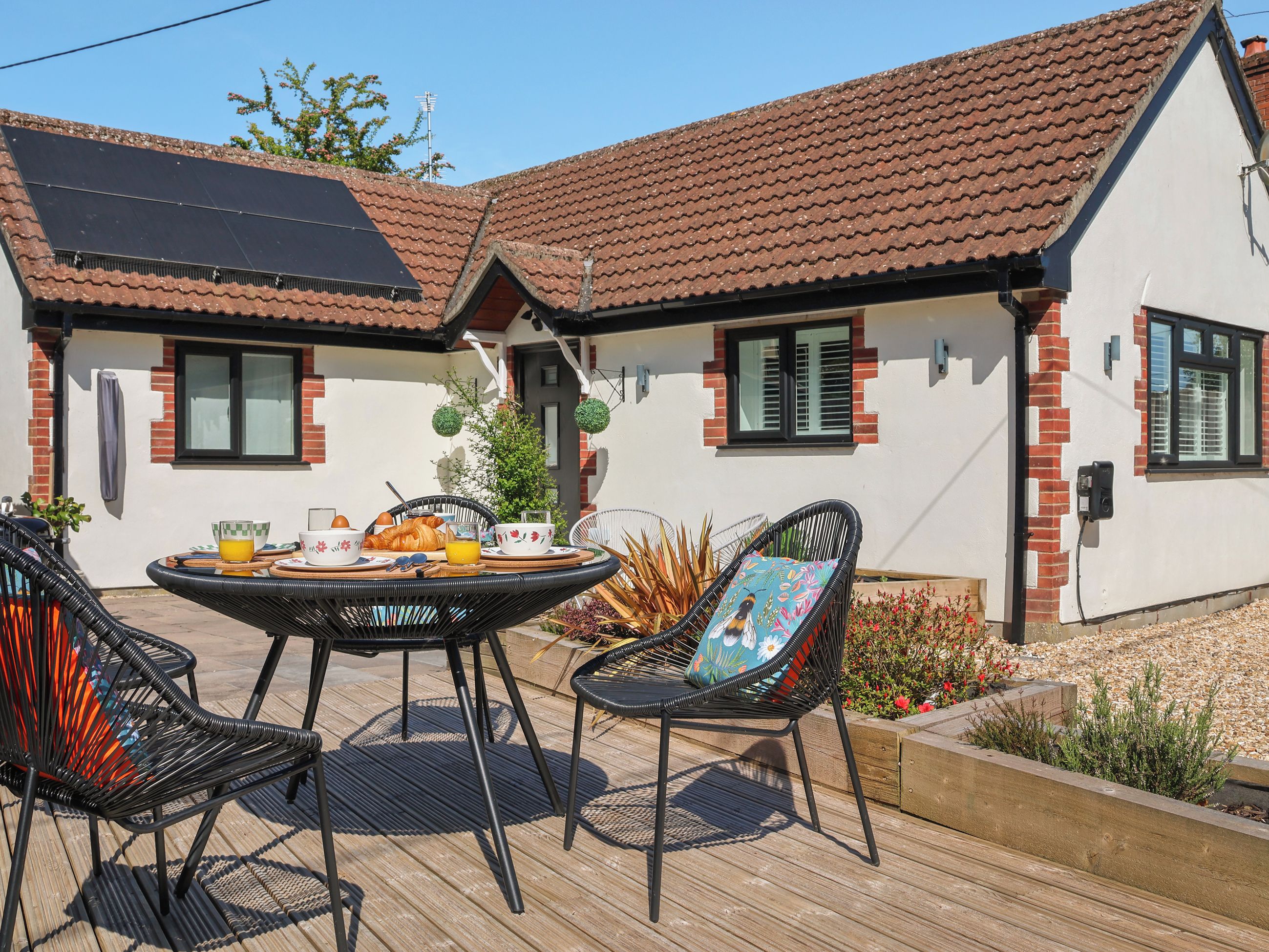 A patio with a table set for breakfast, two wicker chairs, and a small garden area with plants and flowers.