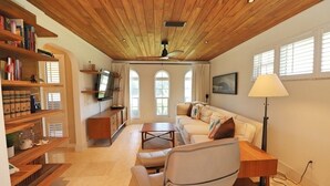A cozy living room with a wooden ceiling, a sofa, a coffee table, and a bookshelf.